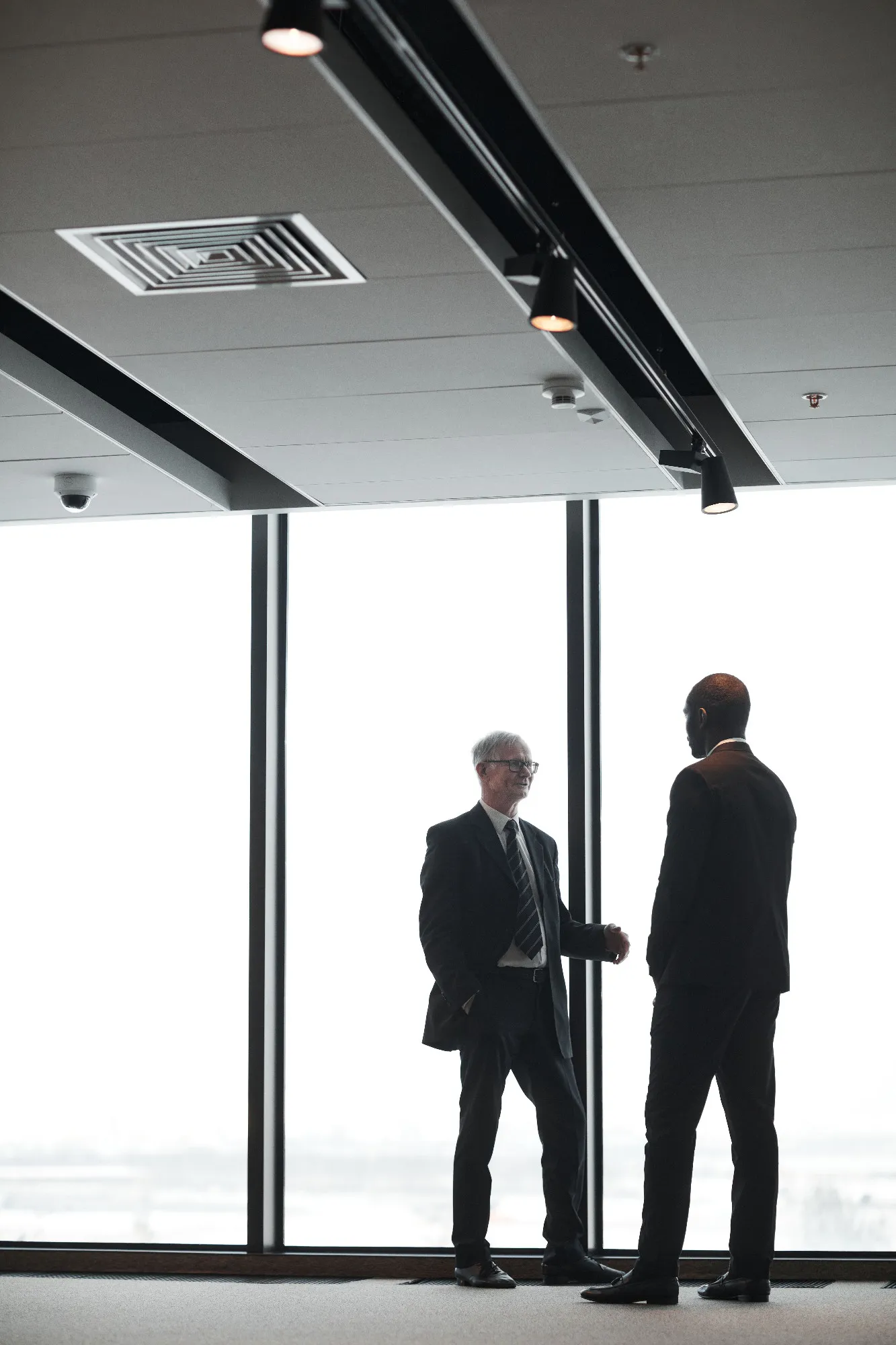Dois profissionais em conversa, silhuetas contra uma janela iluminada em ambiente corporativo